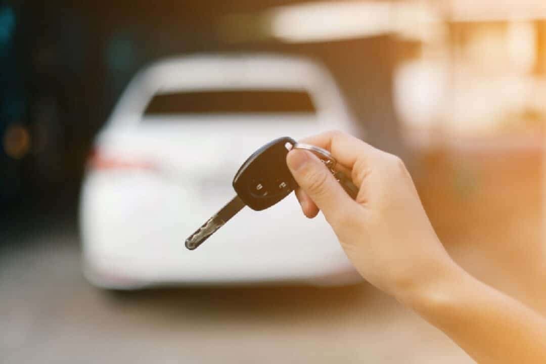 Consórcio de veículos: uma pessoa segura uma chave de veículo e, ao fundo, há um carro branco.