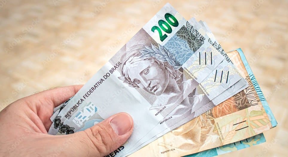 Empréstimo rápido: um homem segura uma nota de duzentos reais, uma nota de cinquenta reais e uma nota de cem reais.