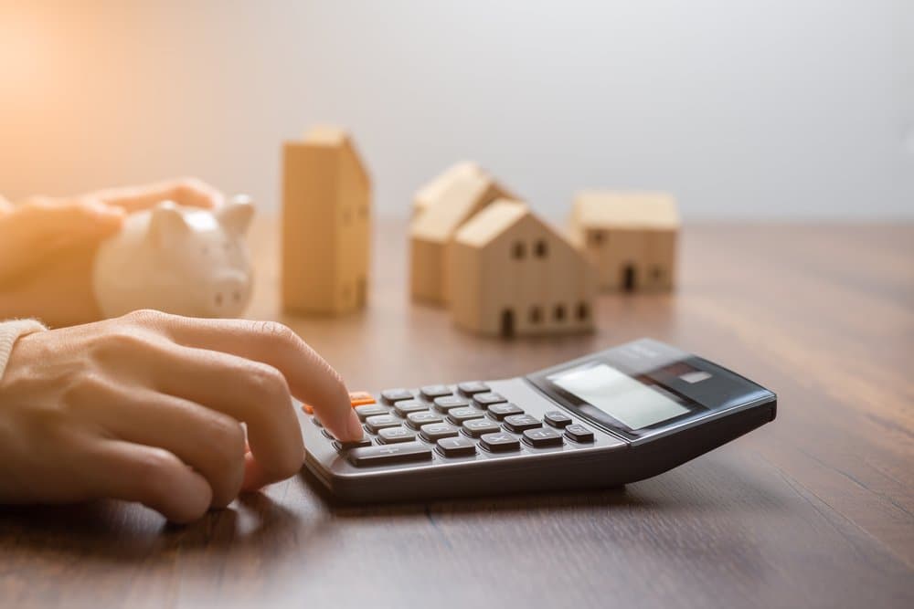 Quebra de acordo: uma pessoa utiliza a calculadora e, ao lado, há miniaturas de residências e de um cofrinho em formato de porco.