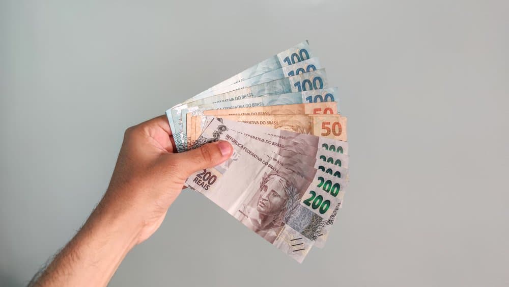 Caderneta de poupança: uma pessoa segura algumas notas de duzentos, cem e cinquenta reais.