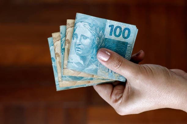 empréstimo: mão segurando bolos de notas de 100 e 50 reais