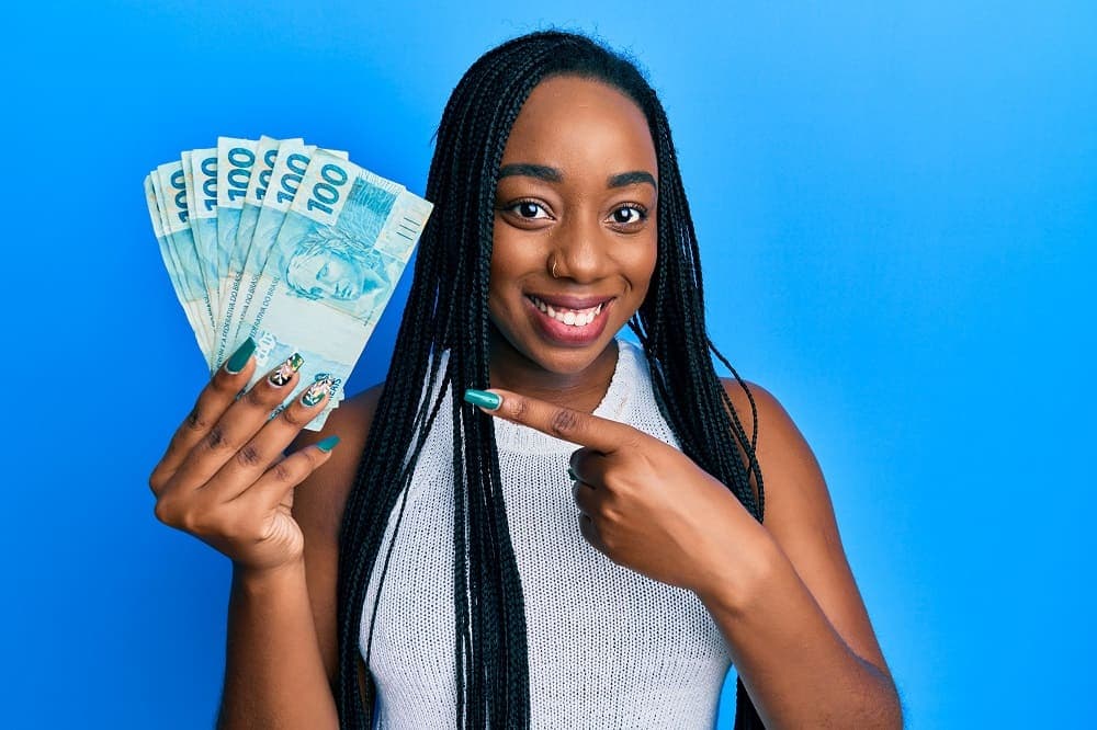 Caixa Tem: mulher sorrindo segurando notas de cem reais