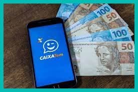 Caixa Tem: celular com a tela exibindo o logo do Caixa Tem e notas de cinquenta e cem reais atrás
