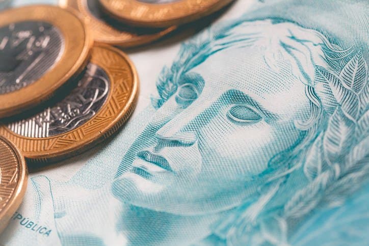 Auxílio Brasil: Nota de cem reais com moedas de um real sobre ela