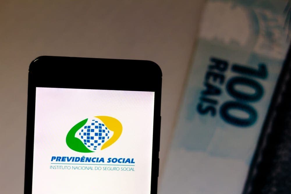 INSS: celular com logo da previdência social e cem reais atrás