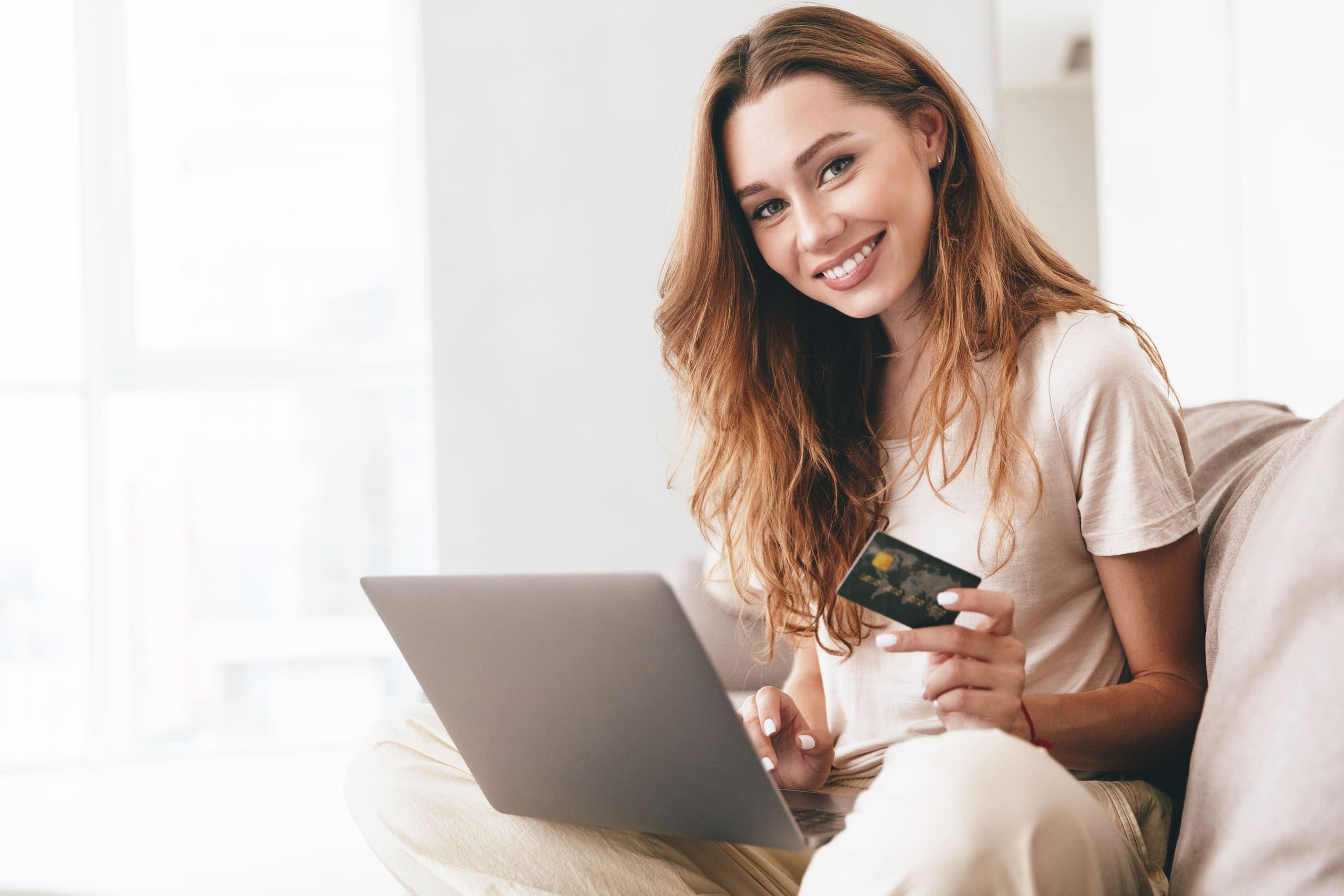 Cartão de crédito: mulher sorrindo segurando cartão em frente ao computador