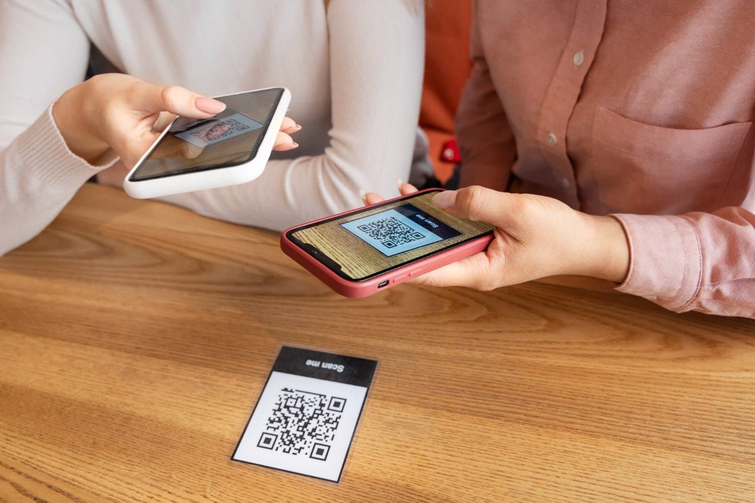 Pix Troco: duas mulheres estão na mesa realizando a leitura de um QR Code através do celular.