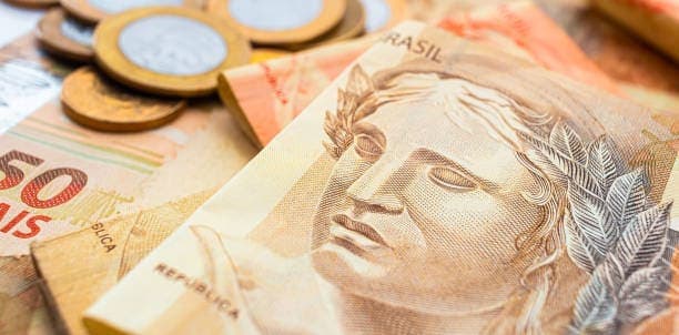 Auxílio Brasil: notas de cinquenta reais e moedas de um real sobre elas