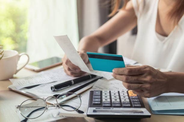 Cartão de crédito: mulher segurando cartão e papel. Calculadora ao lado e óculos também