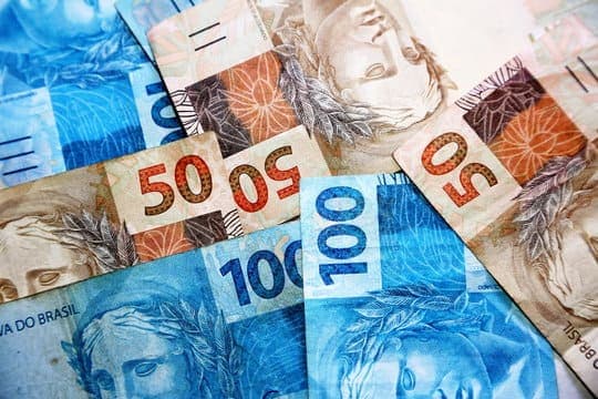 Desafio das 52 semanas: diversas notas de cinquenta e cem reais estão colocadas em uma superfície, umas sobre as outras.