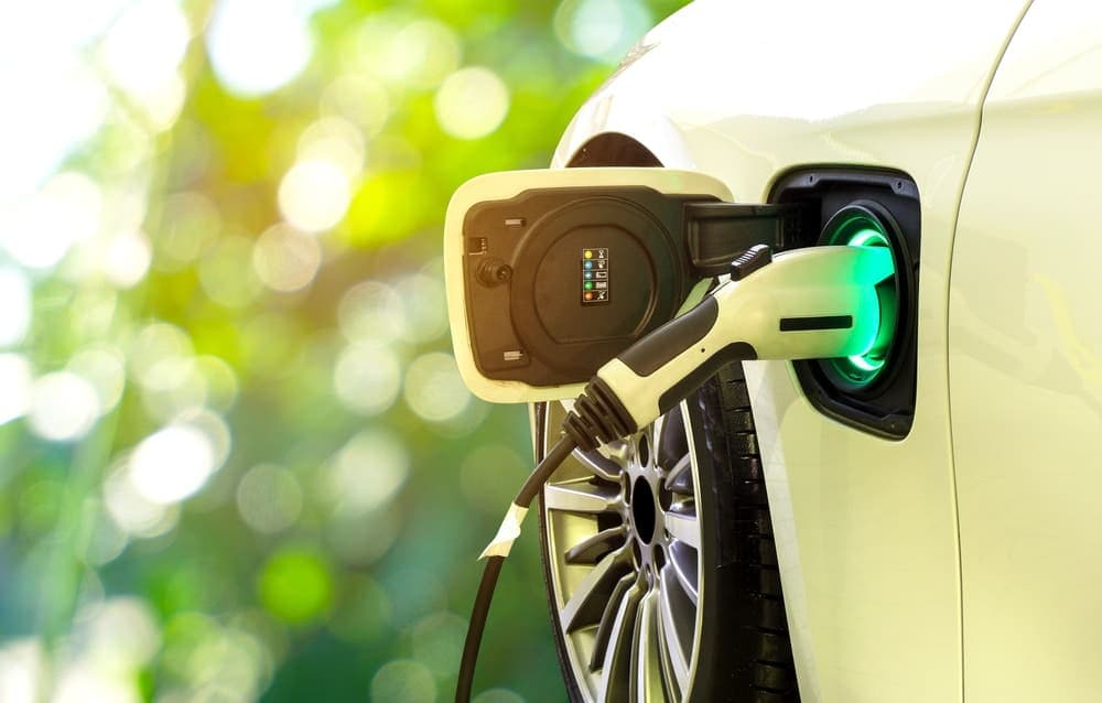 financiamento de carros elétricos: um carro elétrico está sendo carregado. Ao fundo há uma área verde desfocada.