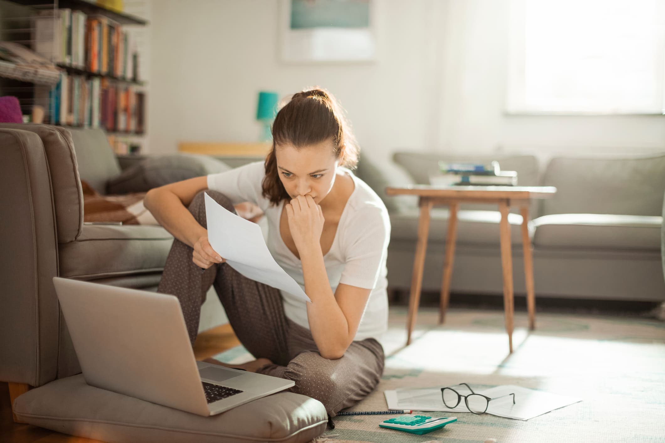 Finanças: uma mulher está sentada no chão, com semblante sério, enquanto lê algo no notebook