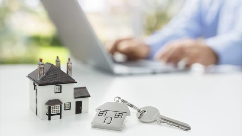 Minha Casa Minha Vida: um homem está no notebook ao fundo, e a frente há uma chave e uma miniatura de residência.