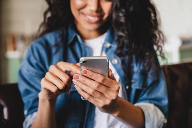 Dicas para contratar um consórcio: uma mulher está mexendo no celular e sorri.
