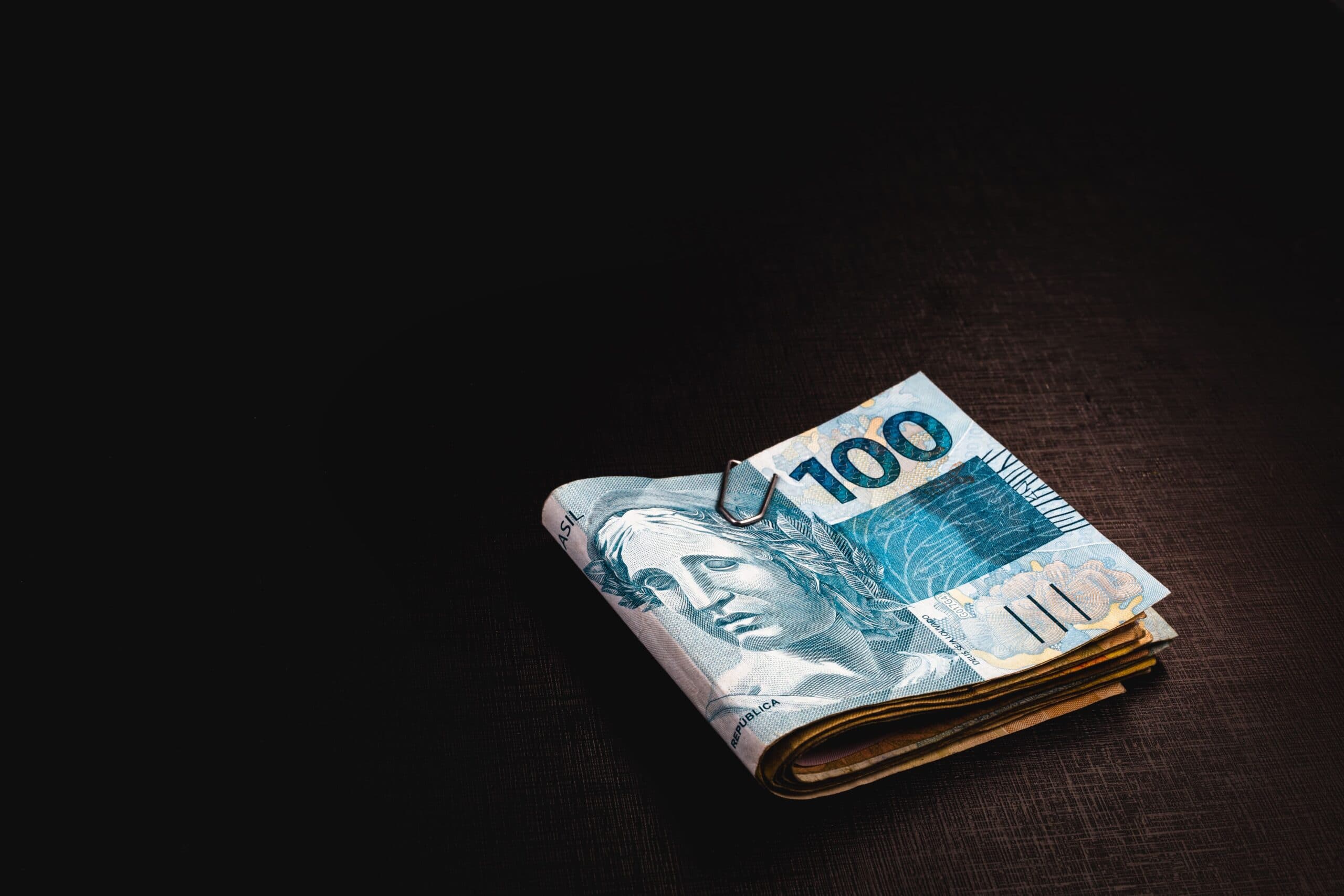 Empréstimo pessoal online: imagem mostra algumas notas de cem reais enroladas entre si, e presas por um clips.