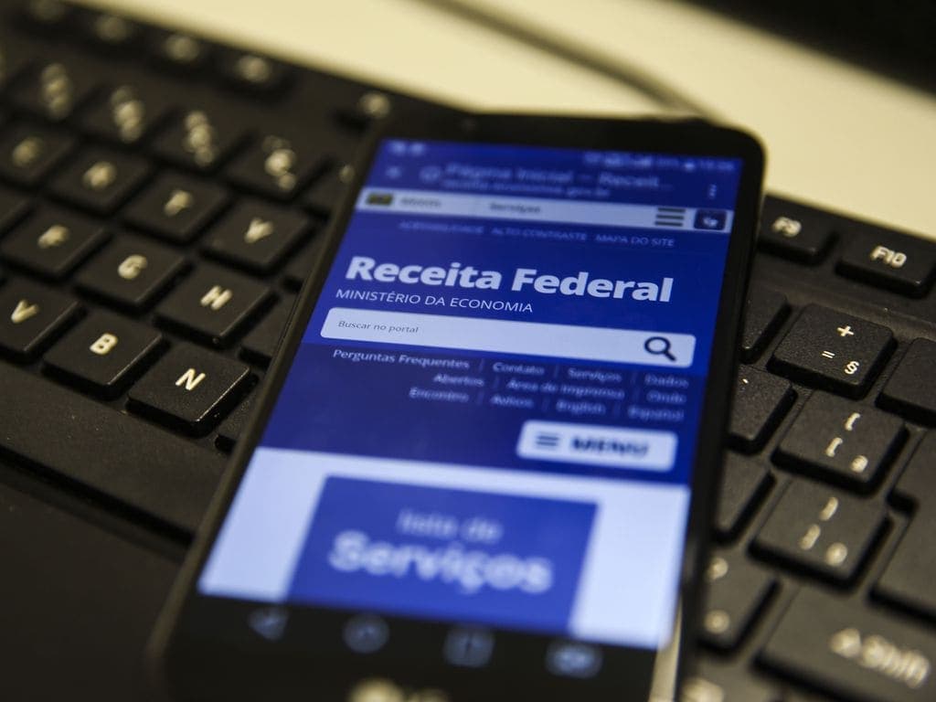 Imposto de Renda: imagem mostra teclado de um computador com um celular em cima. Na tela do dispositivo está o site da Receita Federal.