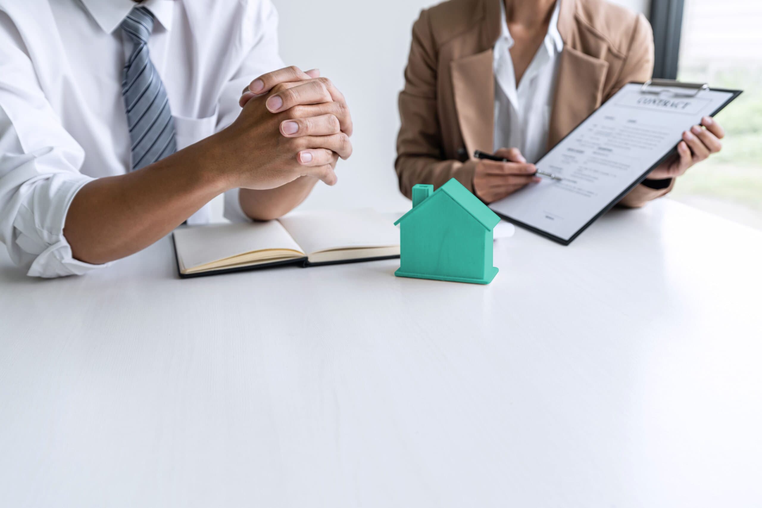 Financiamento de imóvel usado: duas pessoas conversam sobre um contrato. Na mesa, há a miniatura de uma residência em madeira.