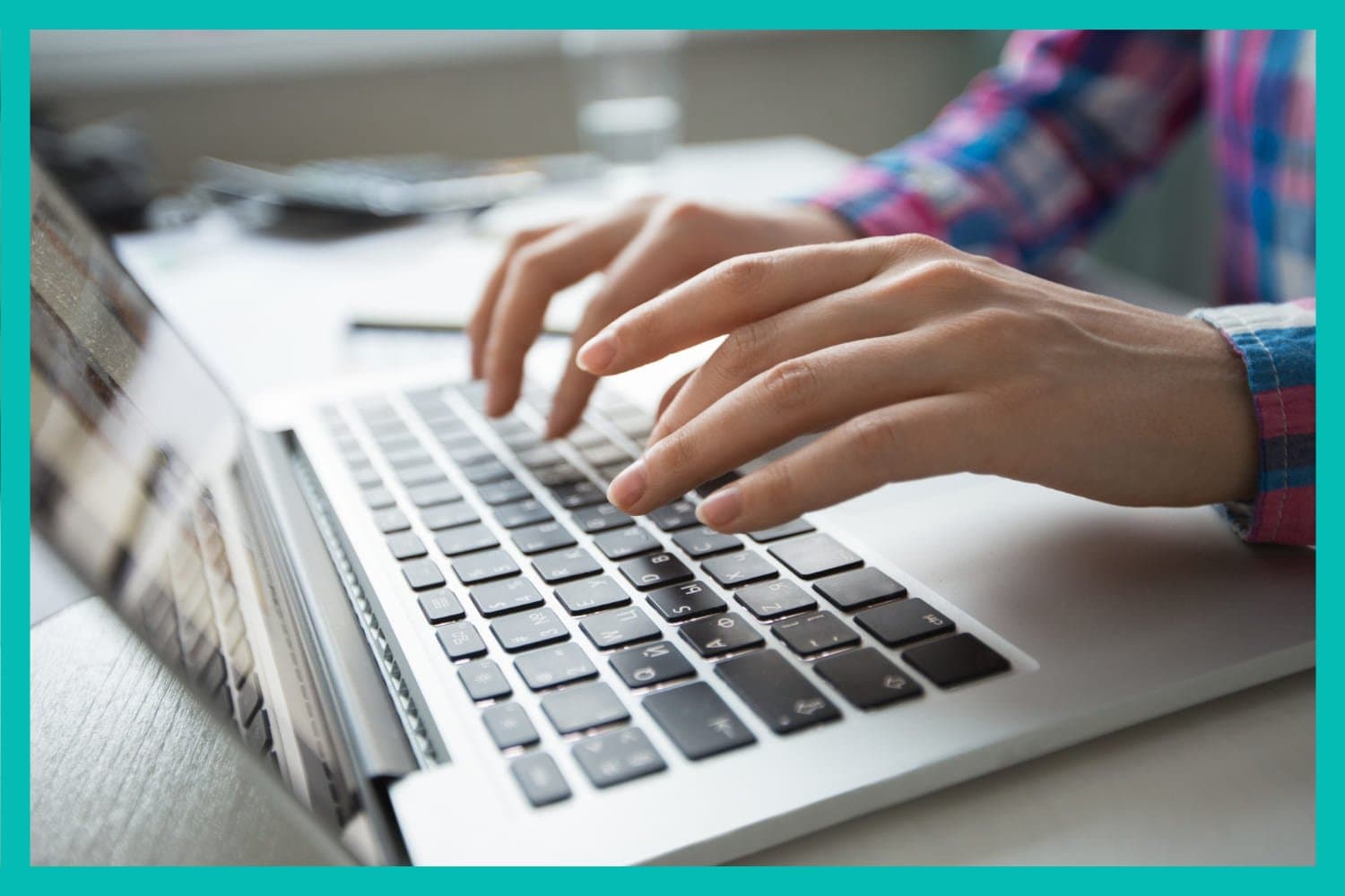 Empréstimo: uma pessoa branca e de camisa xadrez digita em um notebook prata com teclado preto.