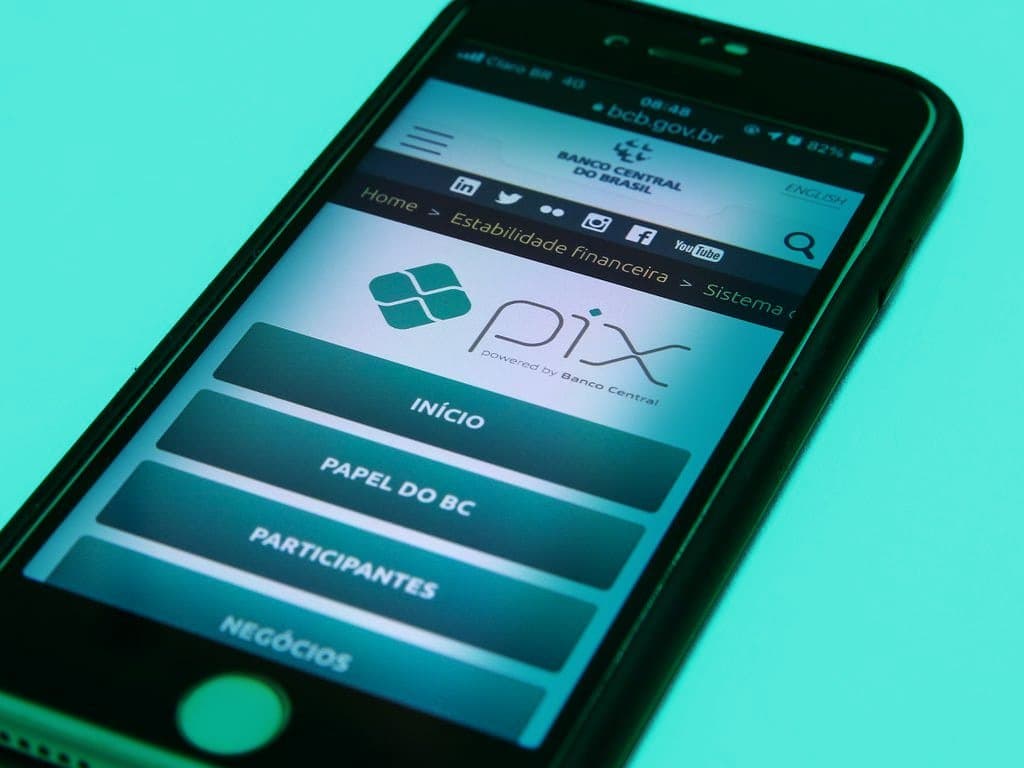 Pix Parcelado: Um celular está numa superfície amarela e, na tela, está o site do Banco Central do Brasil, com o logo do Pix.