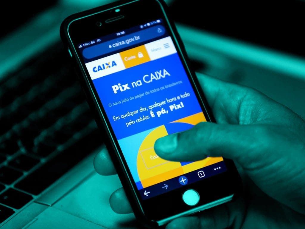 Um homem segura um celular e, na tela, é mostrado o site do Pix da Caixa Econômica Federal.