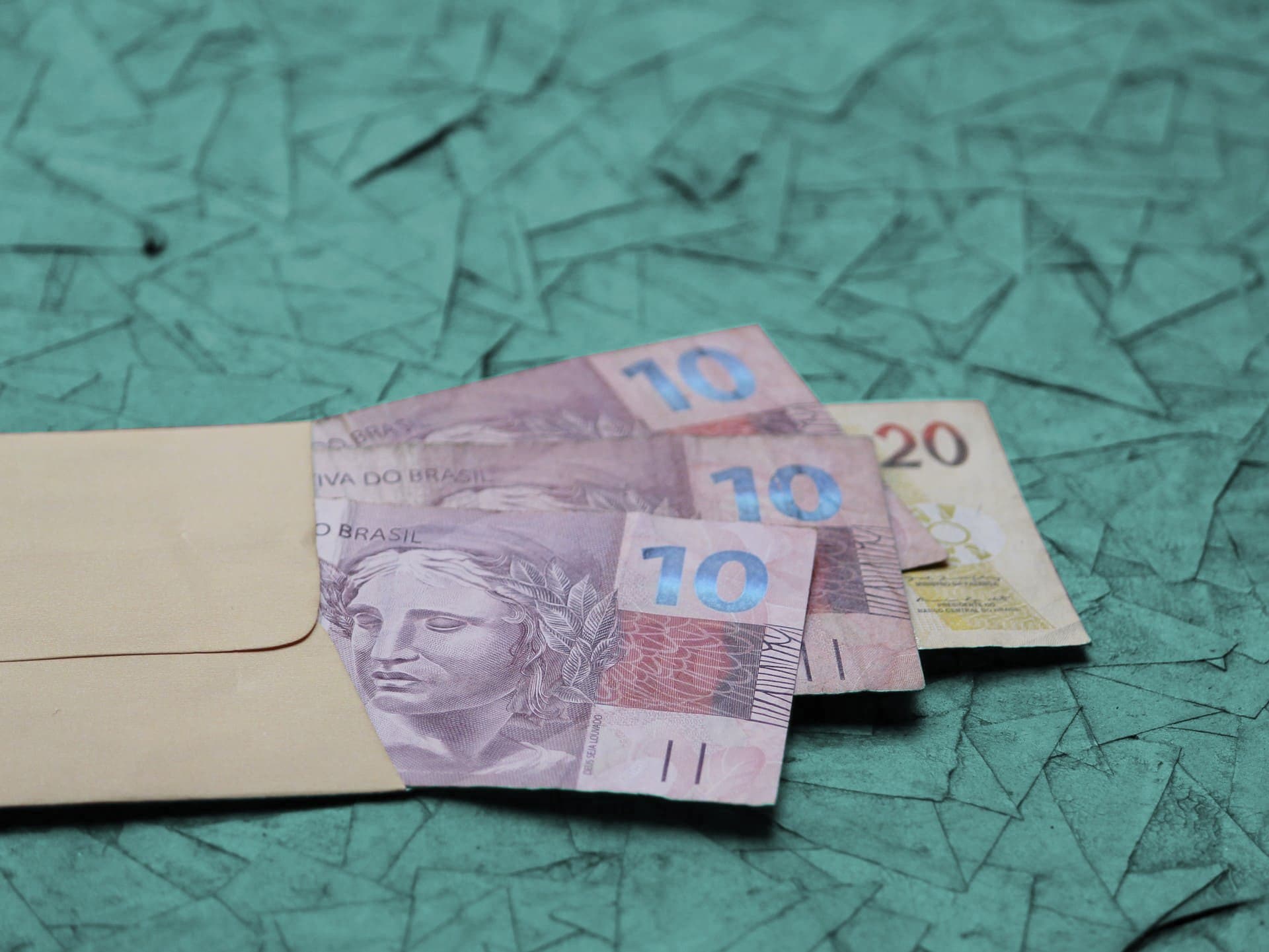 PIS: um envelope aberto contém duas notas de dez reais e uma nota de vinte reais.