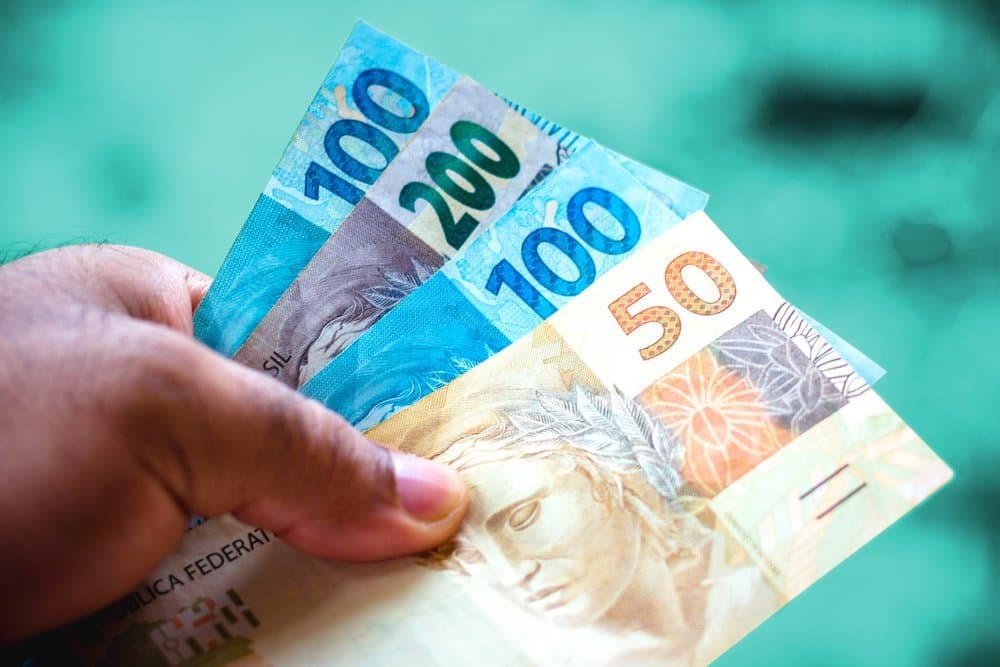 FGTS: mãos masculinas segurando notas de cinquenta, cem e duzentos reais.