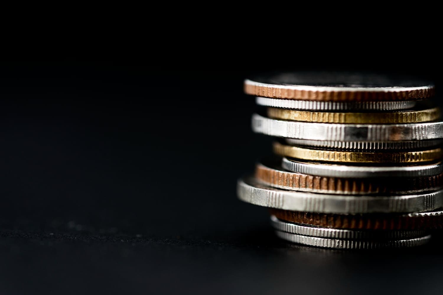 Dinheiro: diversas moedas estão empilhadas, e o fundo da imagem é preto.