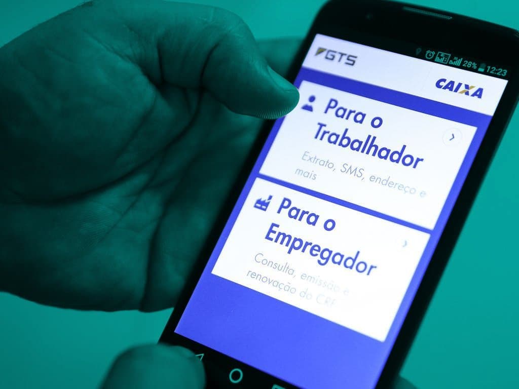 Uma pessoa segura um celular e, na tela, é mostrado o site da Caixa, na aba FGTS para trabalhador e empregador.