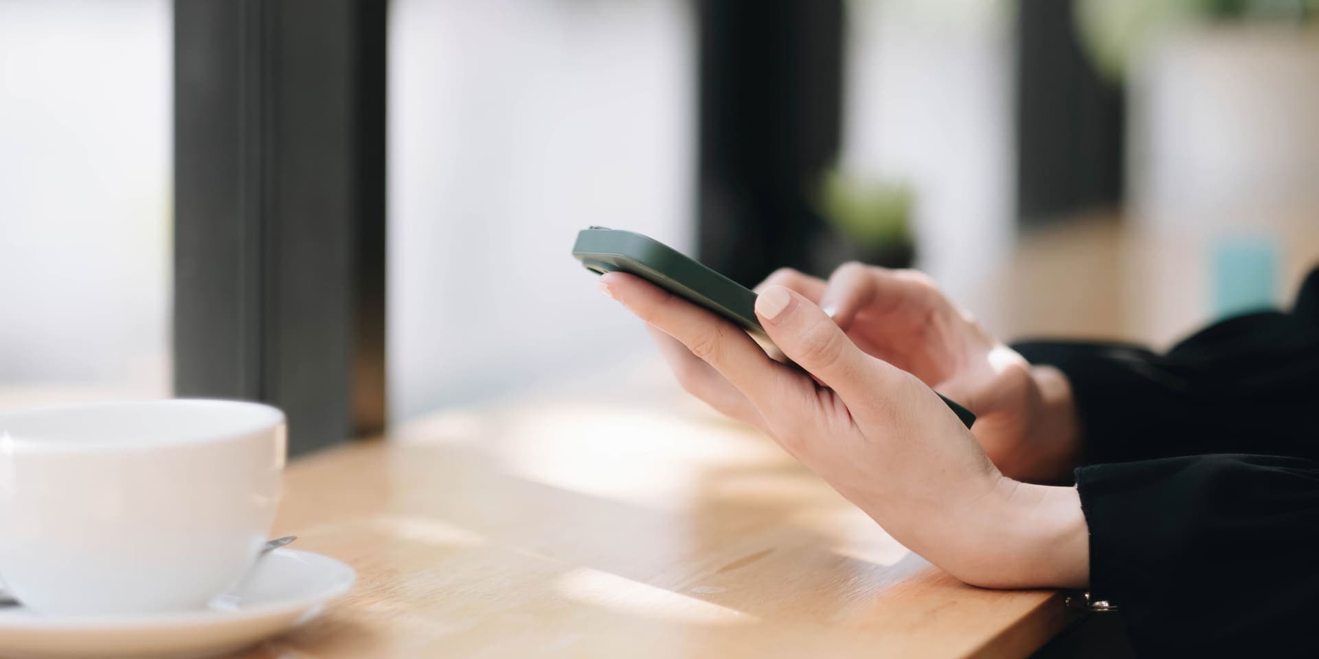 Senha: uma pessoa está sentada na mesa, mexendo no celular e tomando café. (golpe por SMS)