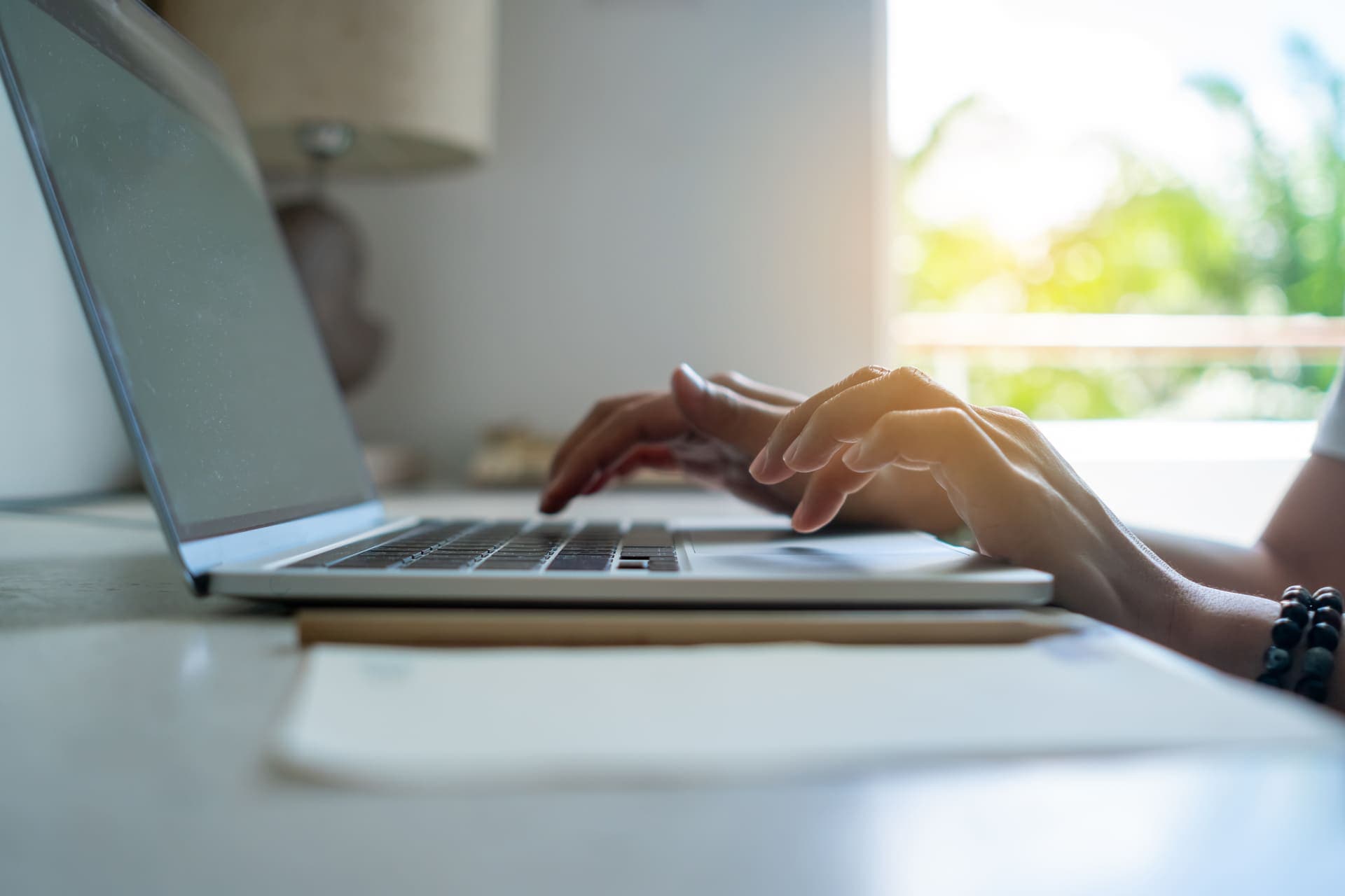 Empréstimo consignado: uma pessoa está sentada à mesa e mexendo no notebook. Ao fundo há uma janela e um abajur.