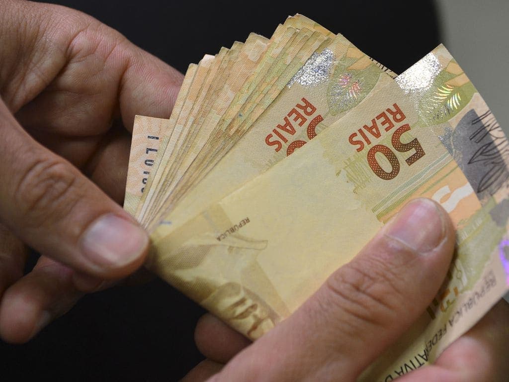 Dinheiro: uma pessoa está contando algumas notas de cinquenta reais.