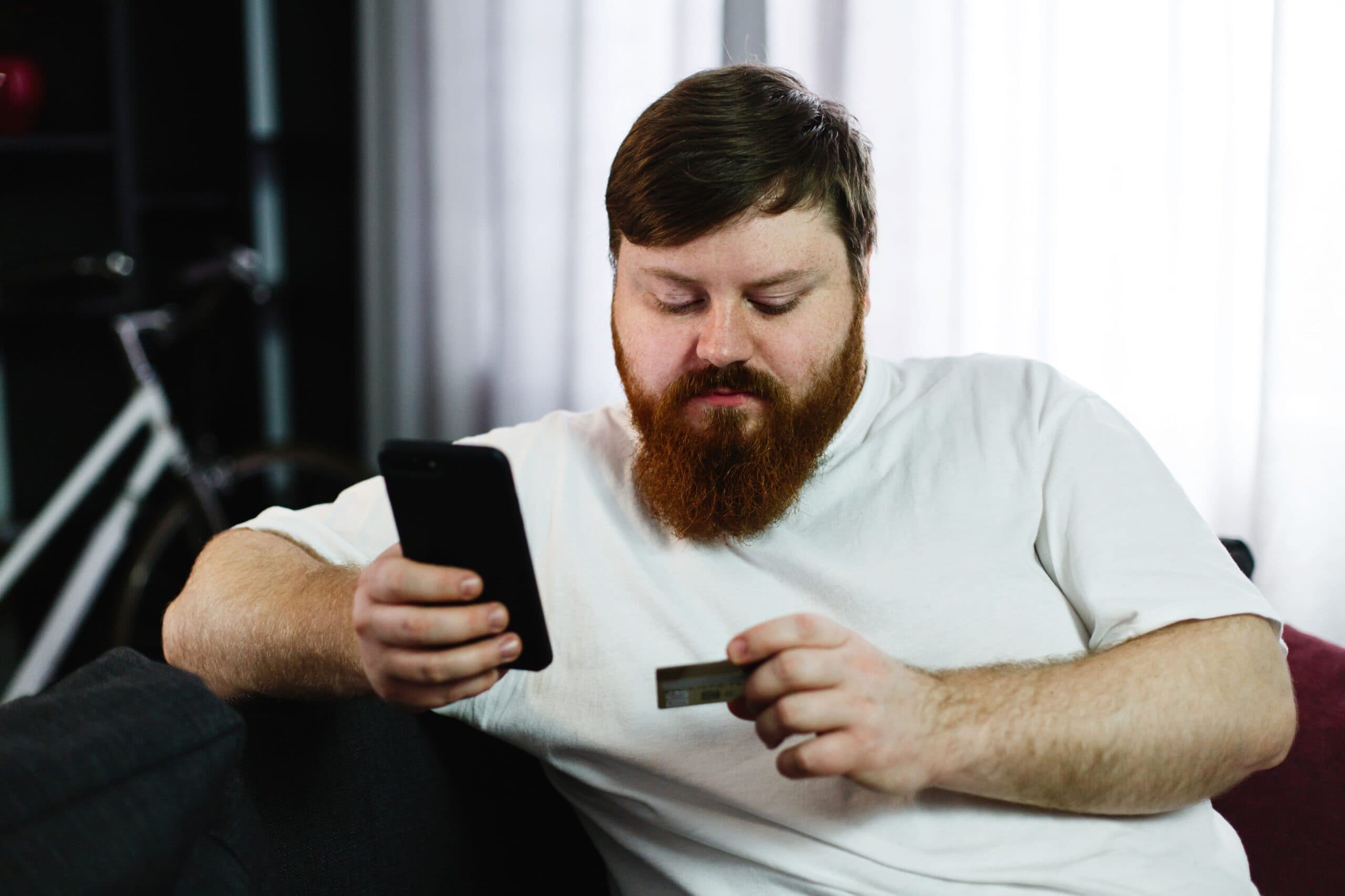 homem segurando celular e cartão (cartão sem anuidade)