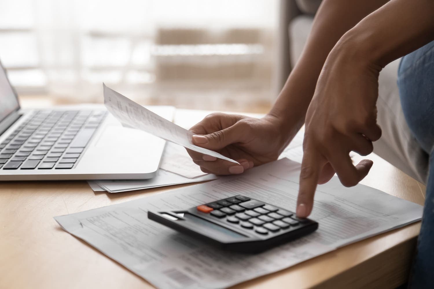 Empréstimo pessoal: uma pessoa utiliza a calculadora com a mão esquerda, enquanto na direita segura um papel. Ao lado há um notebook aberto.