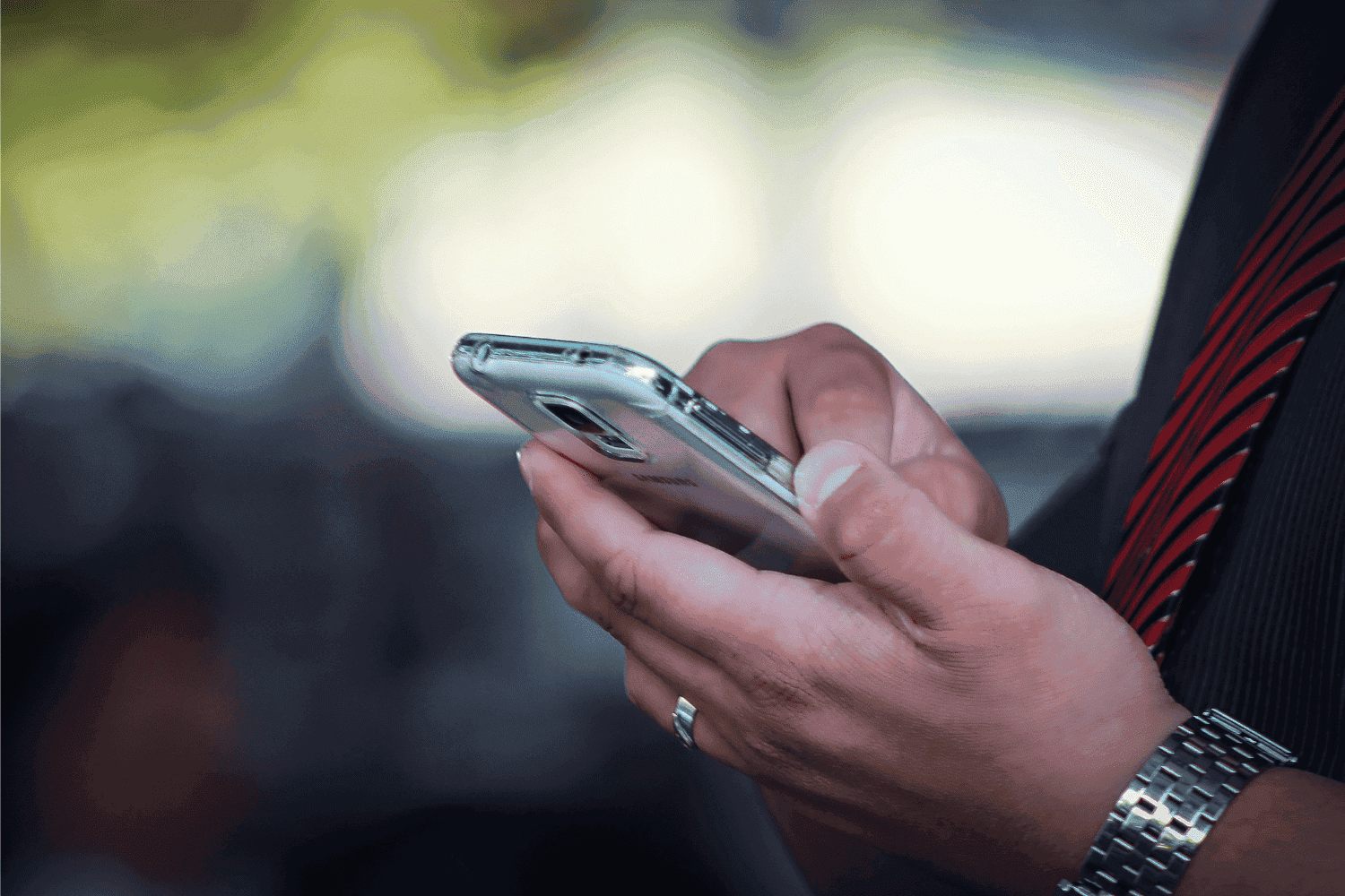 Cartão de crédito: um homem segura um celular enquanto mexe nele. Em seu pulso há um relógio e, no dedo anelar, uma aliança.