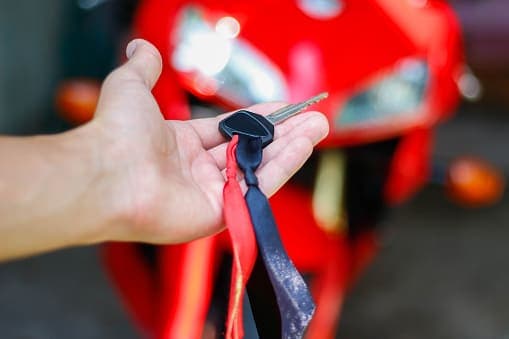 Empréstimo pessoal: uma pessoa segura a chave de uma moto e, ao fundo, está o veículo.