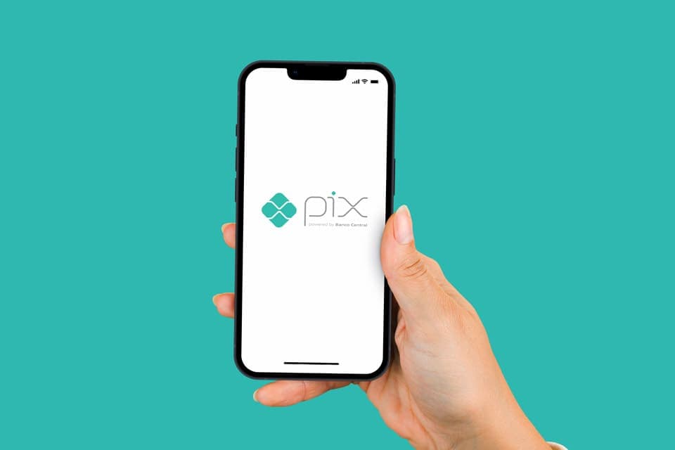 Chave Pix: uma pessoa segura um celular e, na tela, é mostrado o logo do Pix, sistema de pagamentos instantâneos do Banco Central do Brasil.