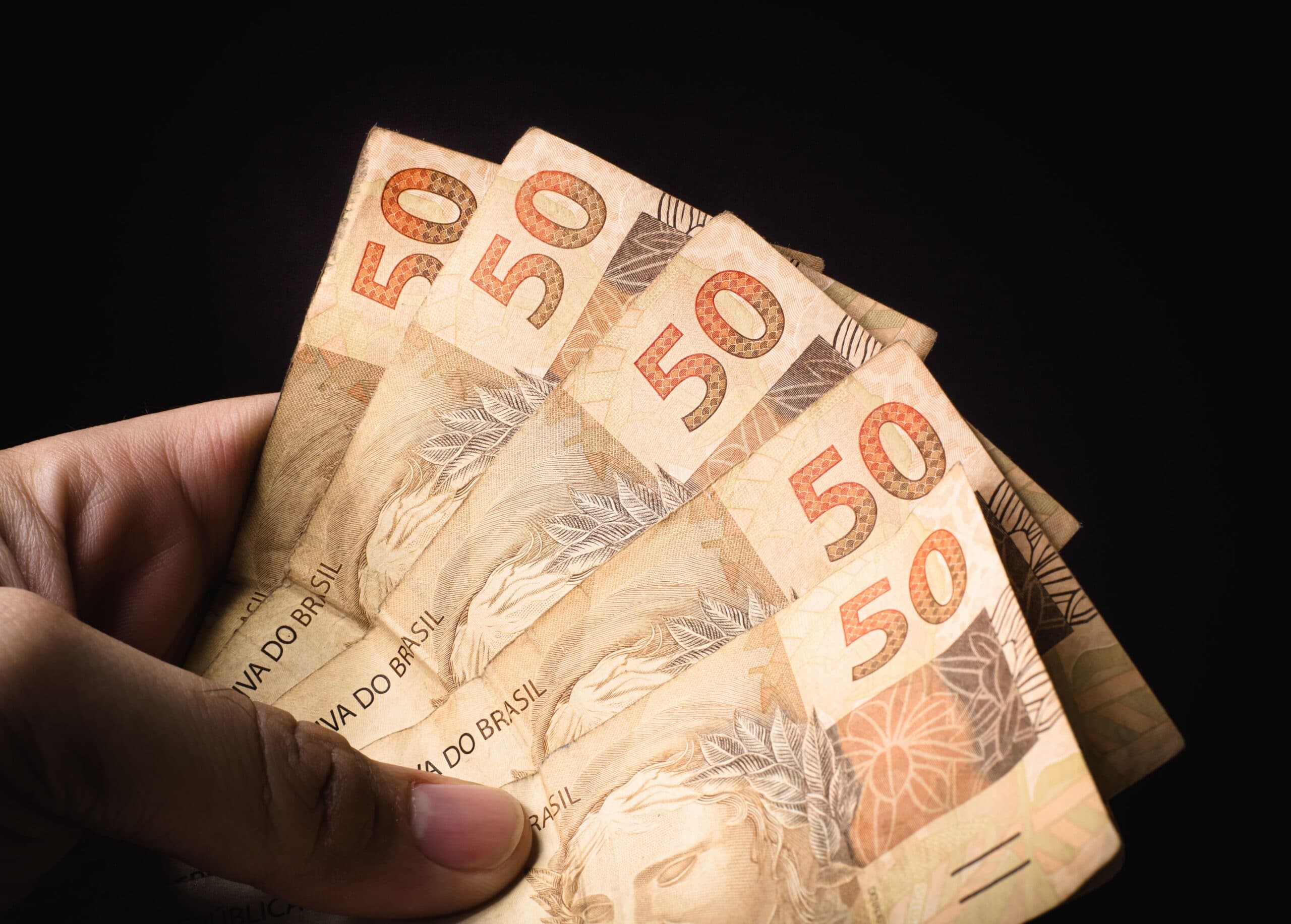 Décimo terceiro proporcional: uma pessoa segura cinco notas de cinquenta reais.