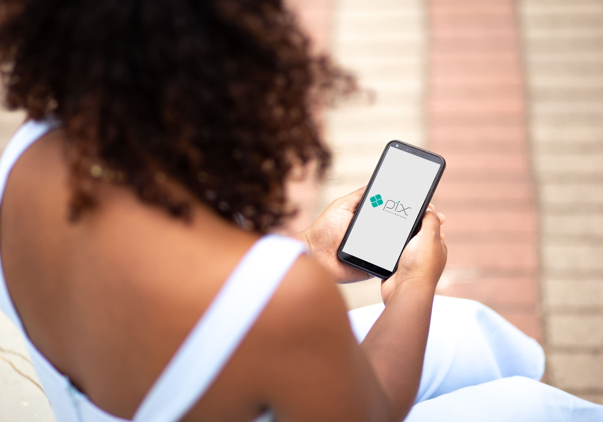 Pix: mulher olhando celular com o logo do pix na tela