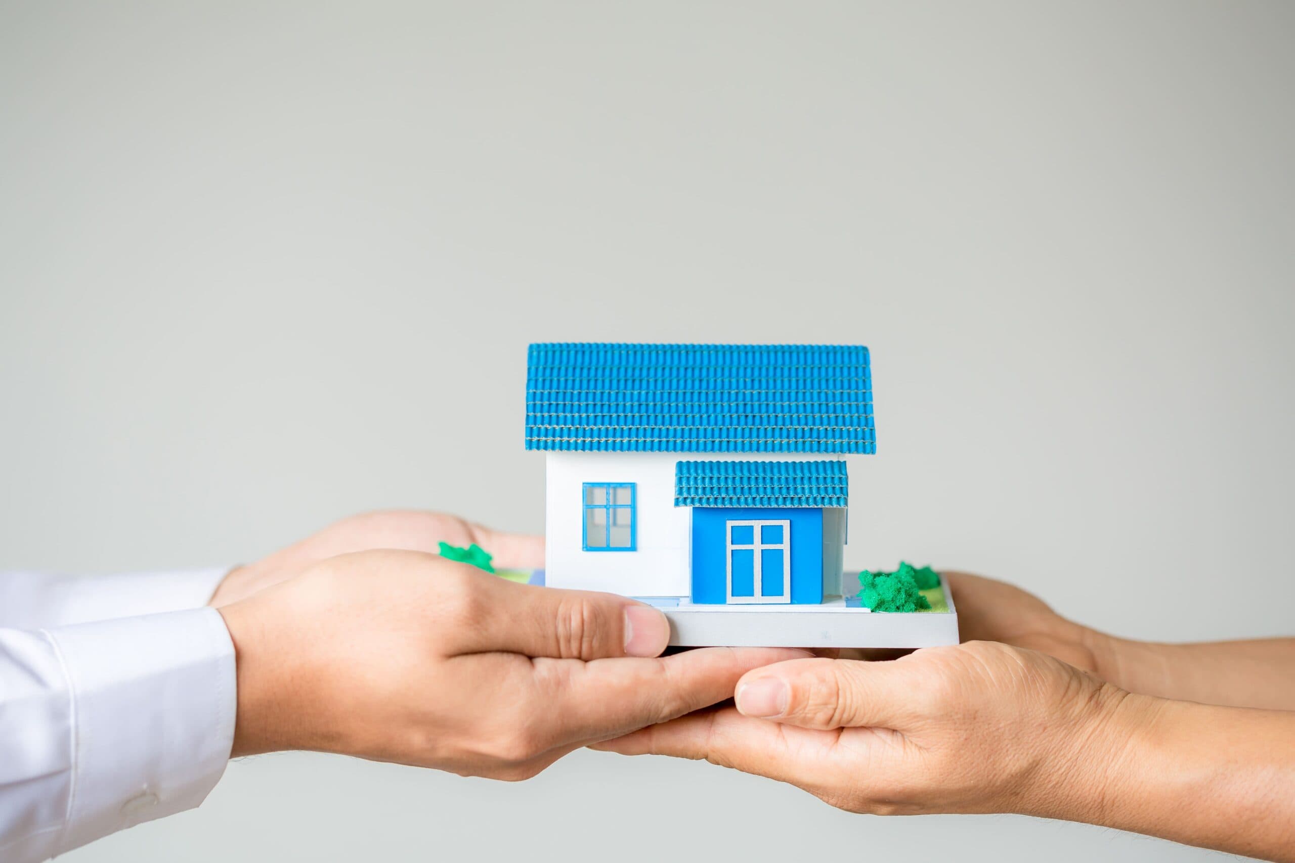duas mãos segurando uma casinha (quitar parcelas de financiamento imobiliário)