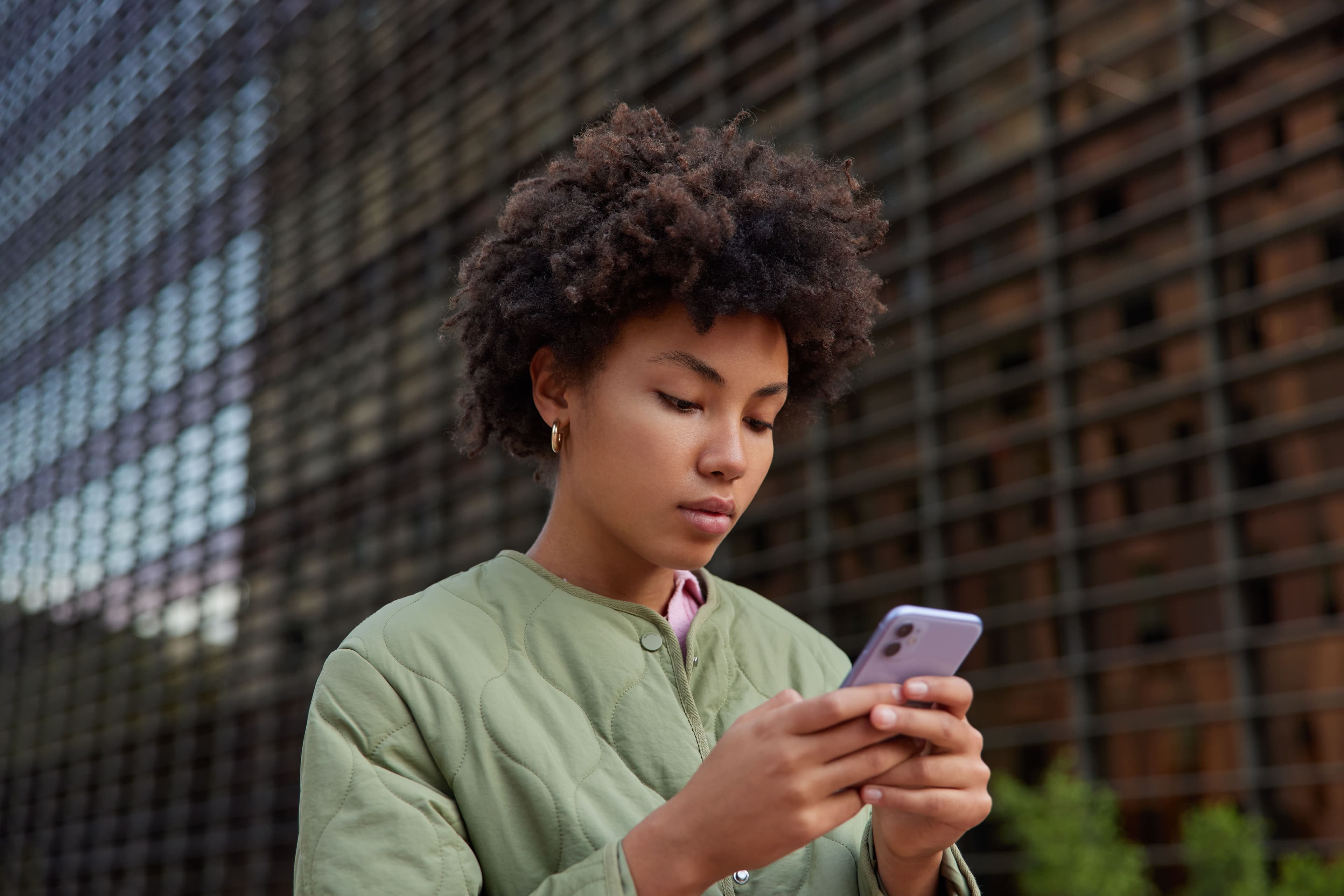 Pix Parcelado: uma mulher está parada na rua, mexendo no celular.