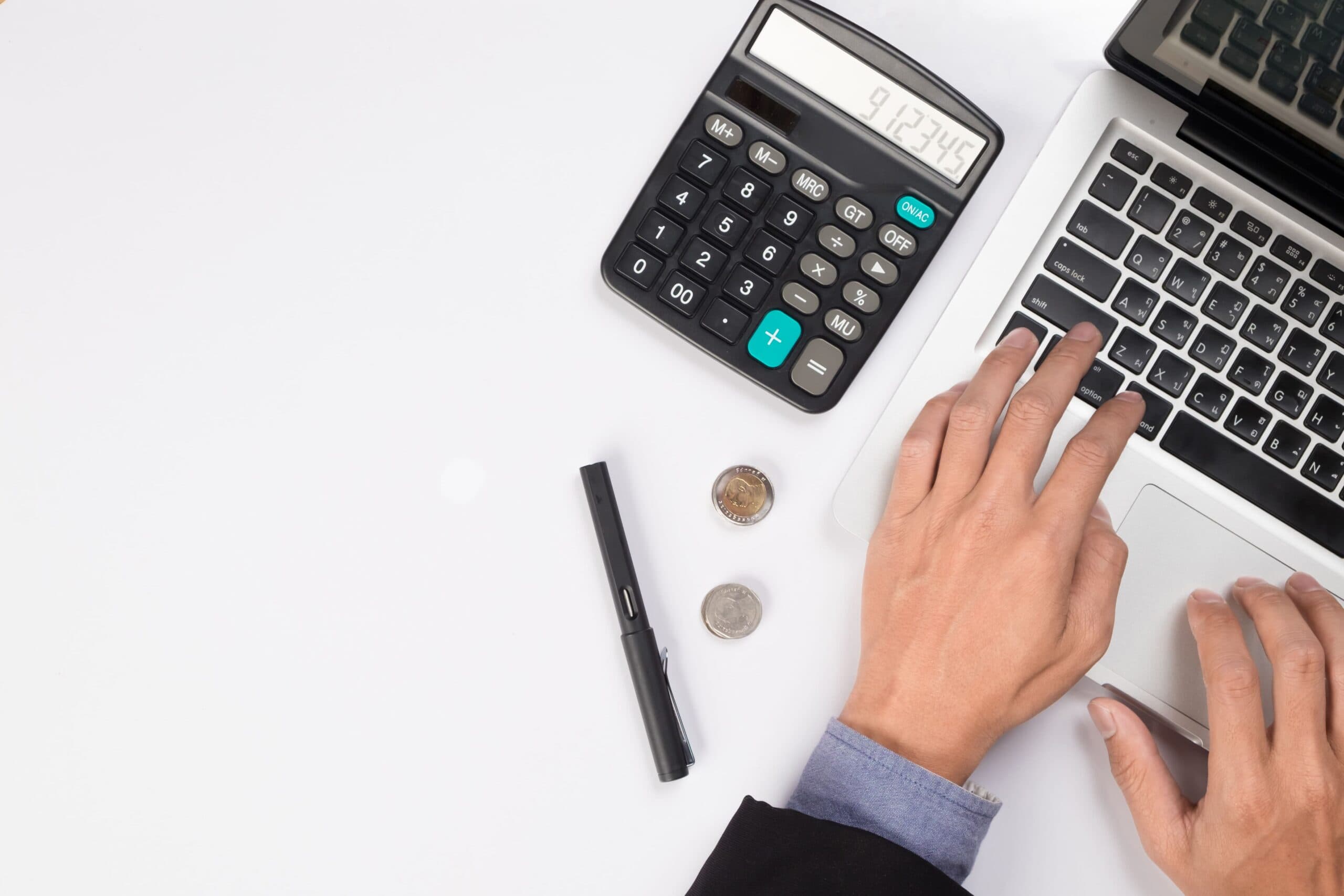 Demonstração do Resultado do Exercício: um homem está utilizando um notebook e, ao lado, há duas moedas, uma caneta e uma calculadora.