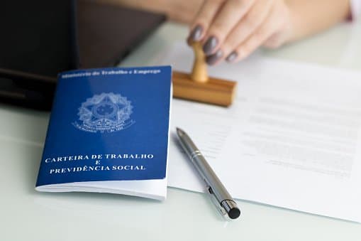 Seguro-Desemprego: uma mulher carimba um documento. Ao lado há uma caneta e a carteira de trabalho.