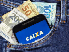 FGTS: celular dentro do bolso da calça jeans com o app da Caixa aberto e notas de 50, 100 e 200 reais atrás