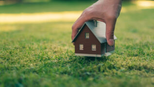 Consórcio de terreno: uma pessoa coloca a miniatura de uma residência em um gramado.