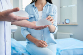 Consórcio para silicone: um médico apresenta diferentes próteses mamárias a uma mulher, que está sentada na maca.