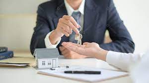 Empréstimo com garantia real: uma pessoa entre as chaves à outra. Na mesa, há uma miniatura de residência e um contrato.