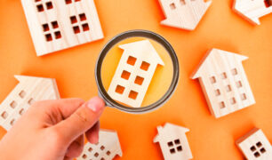 Comprar casa sem entrada: uma pessoa aponta uma lupa para diversas residências em miniaturas.