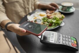 Mulher em restaurante fazendo pagamento com celular em máquina de cartão (Apple Pay)