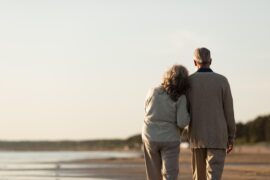 Casal de idosos caminhando na praia (aposentadoria antecipada)
