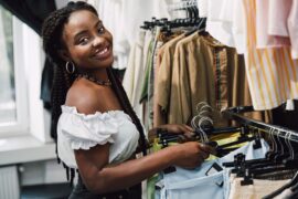 Mulher sorridente em arrumando araras na loja de roupas (faturamento para MEI)